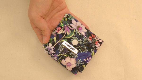 un porte-monnaie porte-cartes en tissu fleuri et doublé en vichy se refermant à l'aide d'un bouton-pression.